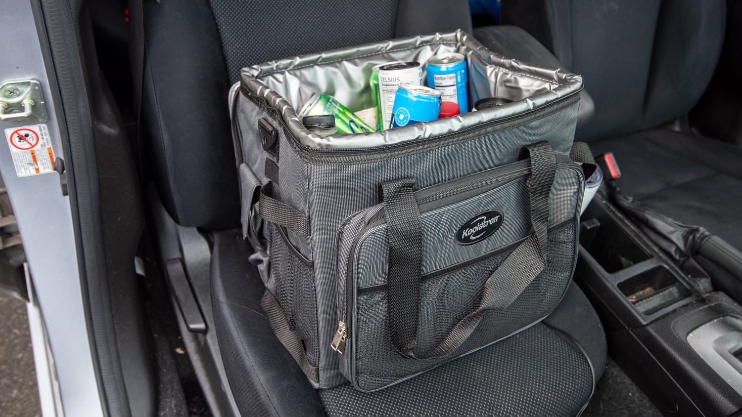A Koolatron D25 sits on the seat of a car, filled with assorted beverage cans