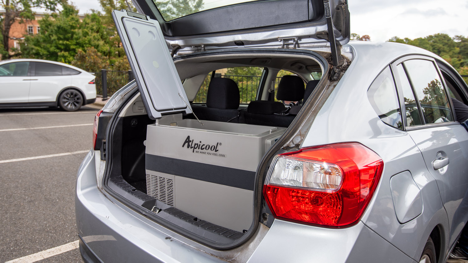 An open Alpicool 12V cooler sits in the open truck of a car